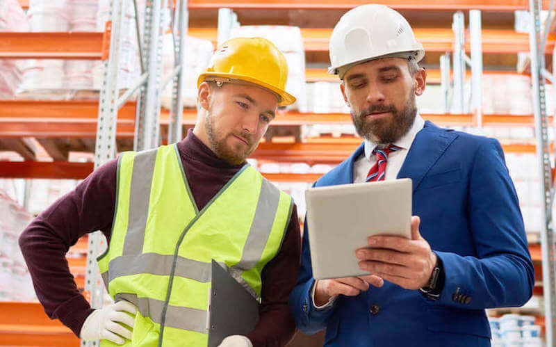 supervisor talking with employee in a warehouse, both looking at a tablet